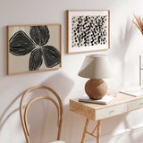 Quadro horizontal com grande flor preta de três pétalas sobre fundo bege, linhas orgânicas marcadas, contraste suave e composição floral contemporânea de estilo depurado. Disponível em kudeko.com