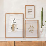 Ensemble de trois tableaux avec visage féminin en ligne continue, formes botaniques et vagues décoratives en beige, sable, taupe et noir, dans un style minimaliste. Disponible sur kudeko.com