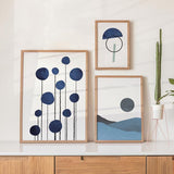 Conjunto de três quadros com formas circulares azuis, linhas finas pretas, semicírculo geométrico e paisagem minimalista em azul, cinzento e preto, num estilo abstrato depurado. Disponível em kudeko.com