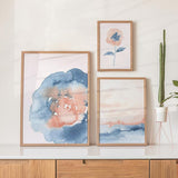 Conjunto de tres cuadros con flor grande azul y rosa, lámina botánica de flor coral con hojas azules y composición suave en tonos pastel, de estilo floral. Disponible en kudeko.com