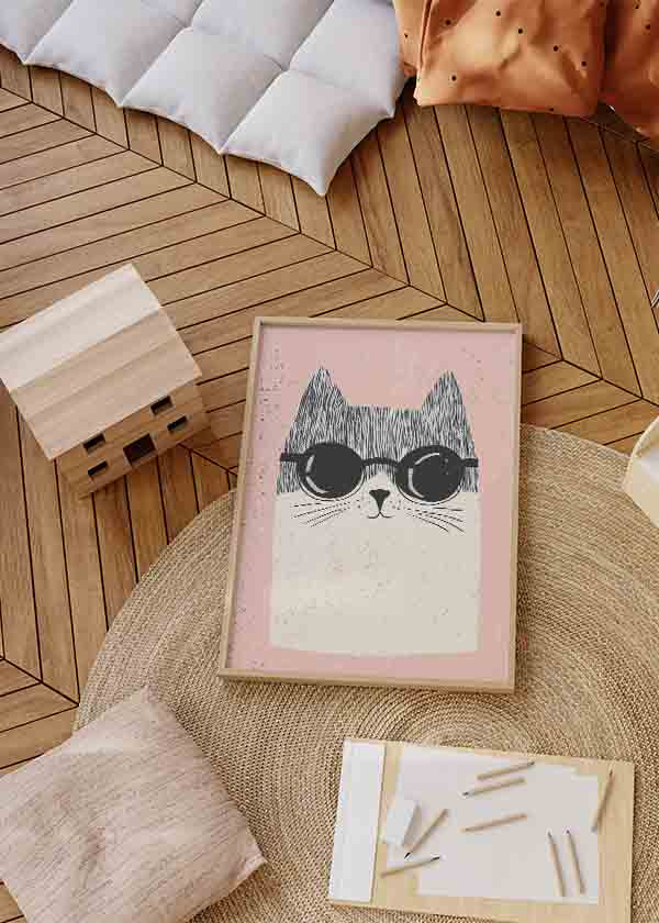 Gerahmtes Wandbild mit schwarz weißer Katze, runder dunkler Brille, puderrosa Hintergrund und kindlichem Stil mit einfachen Formen und freundlichem Ausdruck. Erhältlich auf kudeko.com