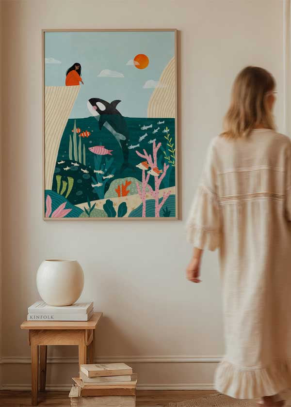 Cuadro ilustrado colorido con orca saltando en el océano frente a una mujer en acantilado, obra de Bea Muller, kudeko.com

