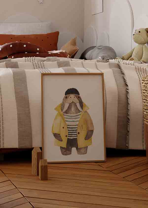 Quadro emoldurado com morsa infantil de impermeável amarelo, gorro preto e camisola às riscas em bege, castanho e cinzento, estilo infantil sobre fundo branco. Disponível em kudeko.com