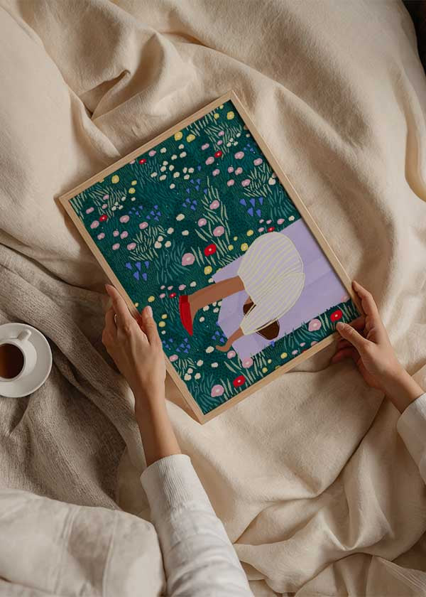 Cuadro ilustrado colorido con mujer descansando en banco lila rodeada de flores silvestres multicolor, obra de Bea Muller, kudeko.com
