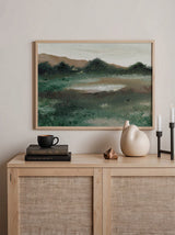 Horizontales Wandbild einer offenen Wiese mit dunklen Sträuchern, Hügeln in Erdtönen, hellem Himmel, graugrünen Nuancen und ruhigem Natur- und Landschaftsstil. Erhältlich auf kudeko.com