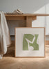 Quadro quadrado com formas geométricas abstratas em verde sálvia sobre fundo bege claro, composição equilibrada de estilo geométrico moderno e depurado. Disponível em kudeko.com