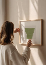 Quadro quadrado com forma botânica abstrata em verde oliva, fundo bege claro texturizado, composição simples e estilo minimalista para decoração de parede contemporânea. Disponível em kudeko.com