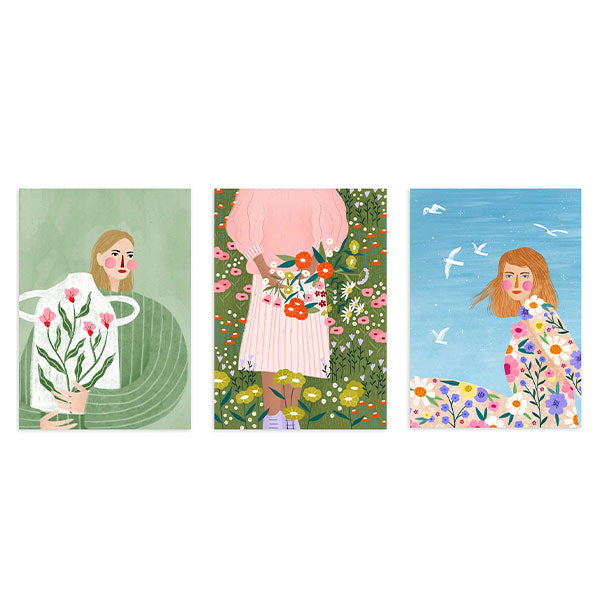 Conjunto de tres cuadros con mujeres entre flores silvestres, vestidos estampados, aves blancas, fondo verde y cielo azul, en estilo ilustración. Disponible en kudeko.com