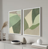 Ensemble de deux tableaux avec formes géométriques organiques superposées en vert sauge, vert mousse, beige et gris pierre, dans un style géométrique équilibré et doux. Disponible sur kudeko.com
