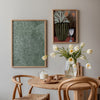 Tableau avec vase cannelé vert olive, branches vert clair, petites fleurs roses, deux fleurs orange, verre blanc, fond brun et style floral contemporain. Disponible sur kudeko.com
