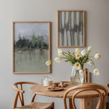 Wandbild mit nebliger Landschaft, verschwommenen Bäumen am Wasser, in Blaugrau, sanftem Grün, Beige und Schwarz, im Natur- und Landschaftsstil gerahmt. Erhältlich auf kudeko.com