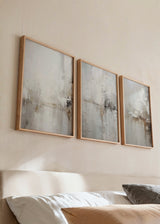 Conjunto de três quadros com composição abstrata em bege, branco pérola, cinzento suave e castanho terra, com texturas difusas, formas irregulares e estilo abstrato equilibrado para decoração de parede. Disponível em kudeko.com