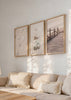 Conjunto de três quadros com conchas marinhas, passadiço de madeira junto ao mar, areia clara, rosa velho, branco, bege suave e estilo fotográfico costeiro. Disponível em kudeko.com