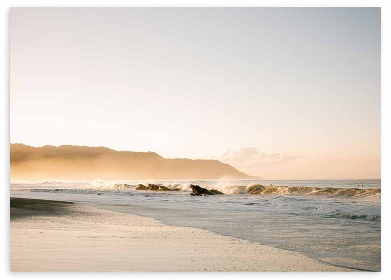Cuadro horizontal de playa en Costa Rica con olas suaves, arena clara, bruma dorada, montañas al fondo y estilo fotográfico en tonos beige y azul grisáceo. Disponible en kudeko.com