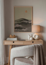 Quadro com montanha escura entre neblina suave, fundo bege, pequeno sol laranja, tons terra suaves e estilo natureza minimalista. Disponível em kudeko.com