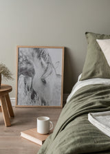 Gerahmtes Wandbild mit hellem Pferd beim Grasen zwischen hohen Gräsern, in Weiß, Grau und Schwarz, mit sanfter fotografischer Bildsprache und natürlichem Stil. Erhältlich auf kudeko.com