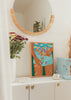 Gerahmtes Wandbild mit weiblicher Figur, türkisfarbenen Shorts, mehrfarbigen Blumen, Schmetterlingen, blauem Hintergrund und illustrativem, dekorativem Stil. Erhältlich auf kudeko.com