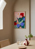 Farbiges illustriertes Wandbild mit Frau, die zwischen großen roten, rosa und violetten Blumen in einer grünen Landschaft geht, von Bea Muller. Erhältlich auf kudeko.com