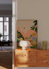 Tableau avec paysage tropical, montagnes roses, rivière bleue, cascade claire, feuillage vert, figures humaines au repos et style illustration aux tons pastel. Disponible sur kudeko.com