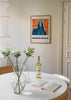 Tableau encadré de la Sagrada Família de Barcelone en tons bleus, entourée de fleurs orange sur fond clair, avec style illustration et composition graphique décorative. Disponible sur kudeko.com