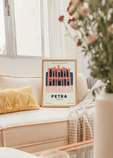 Quadro emoldurado com a fachada de Petra na Jordânia, em tons coral, azul-escuro e rosa suave, com composição arquitetónica em estilo de ilustração, tipografia e coordenadas geográficas. Disponível em kudeko.com