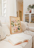 Gerahmtes Wandbild mit rosafarbener Vase, großen Blüten in Cremeweiß und zartem Rosa, grünen Blättern, warmem beigem Hintergrund und floralem Stil. Erhältlich auf kudeko.com