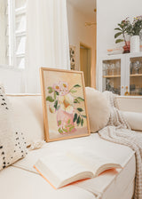 Gerahmtes Wandbild mit rosafarbener Vase, großen Blüten in Cremeweiß und zartem Rosa, grünen Blättern, warmem beigem Hintergrund und floralem Stil. Erhältlich auf kudeko.com