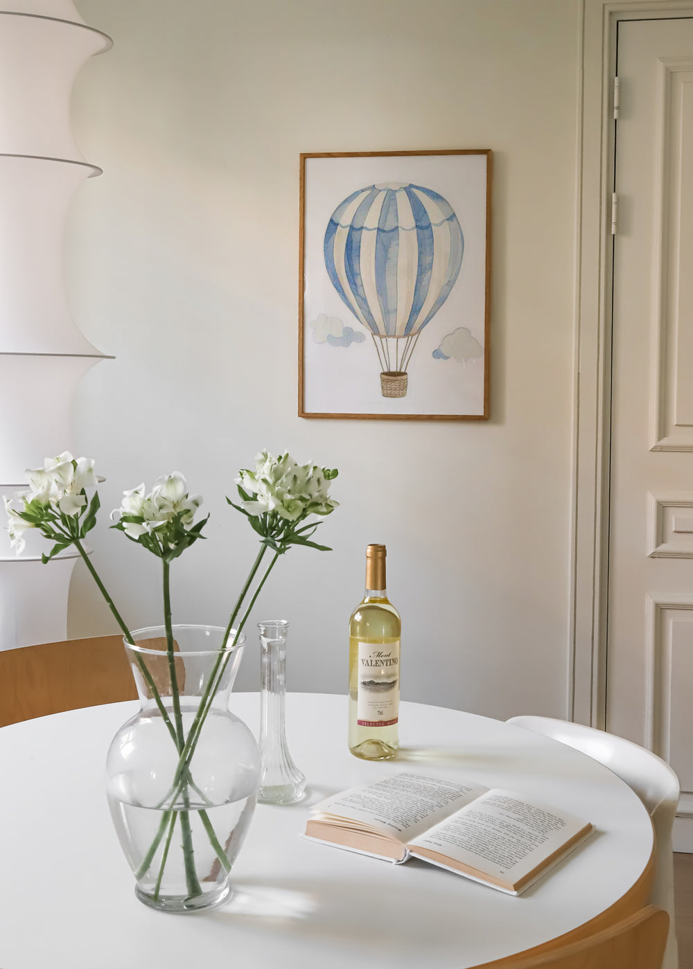 Wandbild mit kindlichem Heißluftballon in blauen und weißen Streifen, kleinen hellen Wolken, beigem Hintergrund und sanftem Stil fürs Babyzimmer. Erhältlich auf kudeko.com