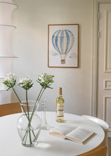 Wandbild mit kindlichem Heißluftballon in blauen und weißen Streifen, kleinen hellen Wolken, beigem Hintergrund und sanftem Stil fürs Babyzimmer. Erhältlich auf kudeko.com