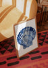 Tableau encadré avec coquillage marin en bleu soutenu et bleu clair sur fond blanc, formes radiales, style illustration et inspiration côtière naturelle. Disponible sur kudeko.com