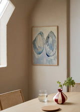 Quadro emoldurado com duas conchas marinhas ovais em azul gelo, branco, cinzento suave e bege, sobre fundo claro, num estilo natureza com inspiração costeira. Disponível em kudeko.com