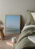 Tableau de plage méditerranéenne avec baigneurs dans l’eau, rochers au bord, mer turquoise, sable clair et grand ciel bleu, dans un style photographique naturel. Disponible sur kudeko.com