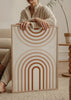 Wandbild mit konzentrischen Bögen und symmetrischen Halbkreisen in Terrakotta, Beige, Creme und Weiß, in einem klaren geometrischen Stil. Erhältlich auf kudeko.com