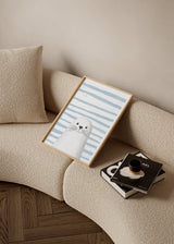 Quadro emoldurado com foca branca de expressão meiga, fundo às riscas azul claro e branco, estilo infantil, composição simples e tons suaves. Disponível em kudeko.com
