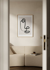 Quadro emoldurado com rosto abstrato em linha preta sobre fundo bege claro, olho circular, nariz curvo, lábios definidos e estilo abstrato minimalista. Disponível em kudeko.com