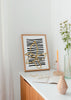 Gerahmtes Wandbild mit großer goldener Linienblüte, unregelmäßigen schwarzen Streifen, weißem Hintergrund und minimalistischem zeitgenössischem Stil. Erhältlich auf kudeko.com