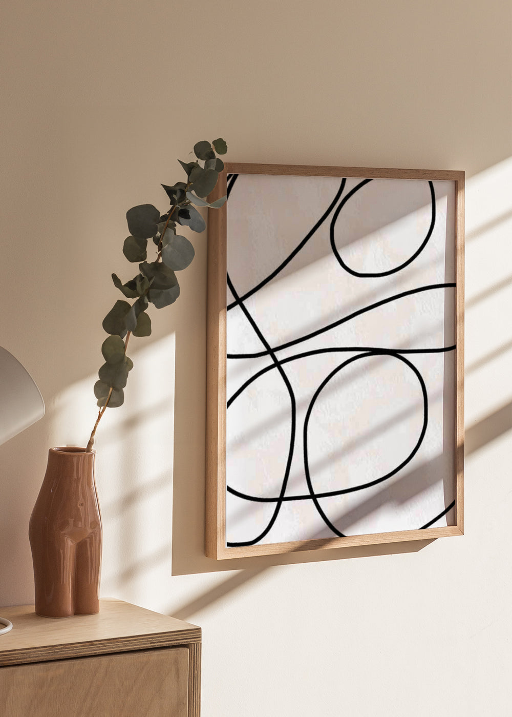 Tableau encadré avec lignes noires courbes entrelacées sur fond blanc cassé, composition abstraite aux formes organiques amples et style minimaliste contemporain. Disponible sur kudeko.com