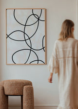 Wandbild mit ineinander verlaufenden schwarzen geschwungenen Linien auf cremeweißem Hintergrund, klare abstrakte Komposition in neutralen Farben und minimalistischem Stil. Erhältlich auf kudeko.com