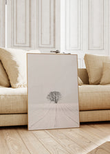 Gerahmtes Wandbild mit einem einzelnen Baum auf weißem verschneitem Feld, sanftem Horizont, grauen und schwarzen Tönen, ruhige Komposition im fotografischen Stil. Erhältlich auf kudeko.com