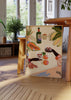 Quadro com cena de brinde, taças de vinho, garrafa, papaia, bananas, uvas e folhagem tropical em tons de creme, verde, laranja e bordeaux, em estilo de ilustração decorativa. Disponível em kudeko.com