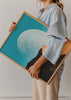 Gerahmtes Wandbild mit großem weißem Mond, türkisfarbenem Himmel, orangefarbener Düne, einsamer Silhouette und dunkler Landschaft im fotografischen surrealen Stil. Erhältlich auf kudeko.com