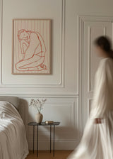 Gerahmtes Wandbild mit sitzender weiblicher Figur in roten Linien, cremefarbenem Hintergrund mit feinen rosa Streifen, im ruhigen zeitgenössischen Illustrationsstil. Erhältlich auf kudeko.com