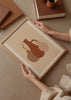 Gerahmtes Wandbild mit drei Vasen in organischen Formen, in Erdtönen, Terrakotta, Beige und Altrosa, auf cremefarbenem Hintergrund, im minimalistischen und klaren Stil. Erhältlich auf kudeko.com