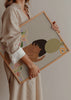 Wandbild mit liegender nachdenklicher Frau, transparentem Kleid mit Blumenmuster, grüner Vase mit korallenfarbenen Blumen, beigem Hintergrund und illustrativem Stil. Erhältlich auf kudeko.com