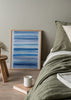 Gerahmtes Wandbild mit horizontalen Streifen in Himmelblau, Hellblau und Dunkelblau auf weißem Hintergrund, in einem klaren abstrakten Stil mit küstennaher und mediterraner Wirkung. Erhältlich auf kudeko.com