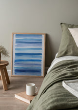Gerahmtes Wandbild mit horizontalen Streifen in Himmelblau, Hellblau und Dunkelblau auf weißem Hintergrund, in einem klaren abstrakten Stil mit küstennaher und mediterraner Wirkung. Erhältlich auf kudeko.com