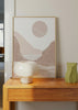 Quadro com paisagem costeira abstrata, sol redondo, colinas em bege rosado, areia clara e linhas onduladas brancas sobre fundo suave, num estilo abstrato equilibrado. Disponível em kudeko.com