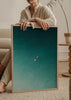 Wandbild mit einsamem Surfer auf weißem Surfbrett in türkisfarbenem und blaugrünem Meer, mit Luftperspektive und klarer Bildsprache im fotografischen Stil. Erhältlich auf kudeko.com