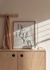Quadro emoldurado com a frase Be Here Now em tipografia serif preta sobreposta sobre fundo bege claro, composição limpa de estilo textual contemporâneo e equilibrado. Disponível em kudeko.com