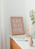 Cuadro decorativo de estilo minimalista y nórdico colocado en salón, frase tipográfica romántica en rosa empolvado, modelo Love Lives Here